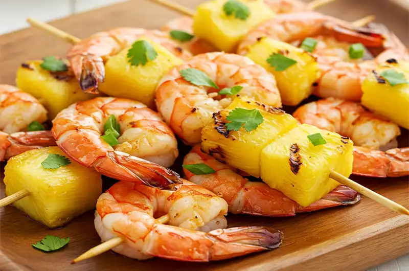Perfectly grilled shrimp and pineapple skewers glistening with glaze and garnished with fresh herbs.