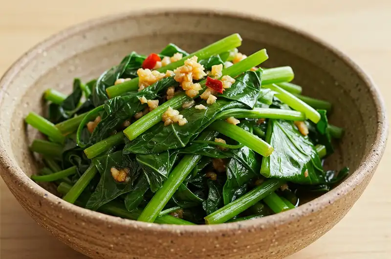 Close-up of sautéed sweet potato leaves with garlic in a ceramic bowl, a simple and nutritious leafy green dish.