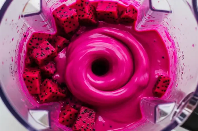 Action shot of red dragon fruit pieces being blended into a smooth, vibrant magenta purée inside a blender pitcher.
