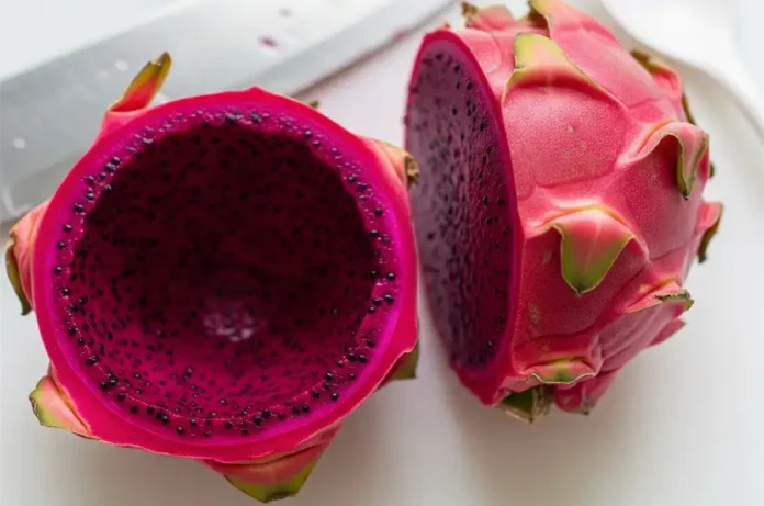 Sliced red dragon fruit clearly showing the inedible skin being separated from the edible flesh.
