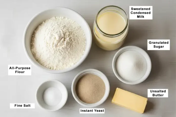 Neatly arranged ingredients for the red dragon fruit bread dough: a bowl of flour, can of condensed milk, small bowls of sugar and salt, yeast packet, and softened butter.