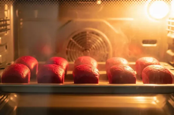 View through an oven door showing red dragon fruit bread loaves baking, turning a beautiful golden-pink color and rising perfectly.