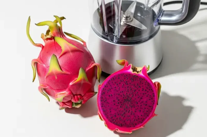 A whole fresh red dragon fruit and a halved one showing its vibrant flesh, placed next to a clean blender, ready for making purée for the bread recipe.